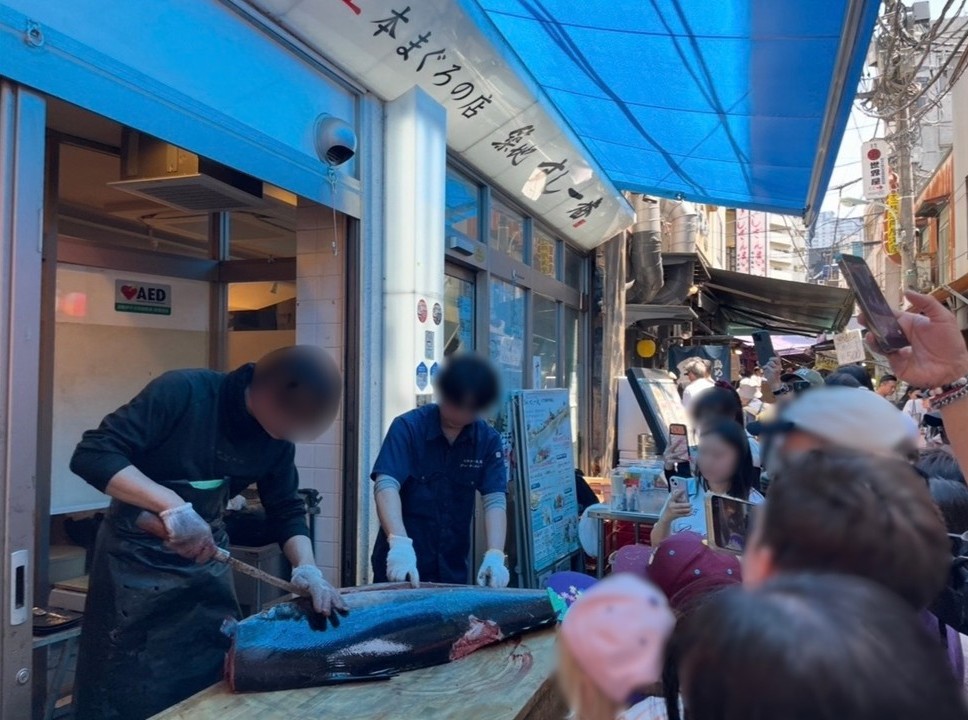 築地場外市場的鮪魚解體秀，職人分切巨型鮪魚，周圍民眾圍觀拍攝。