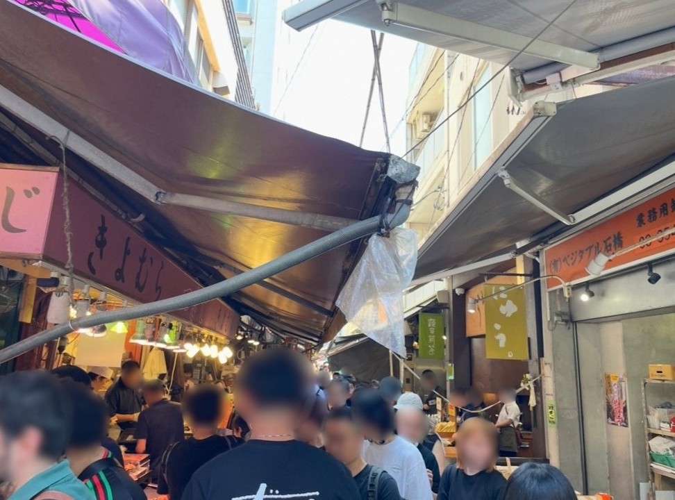 築地場外市場的街景，兩側是餐飲與食材店舖，人潮穿梭的熱鬧市場氛圍。