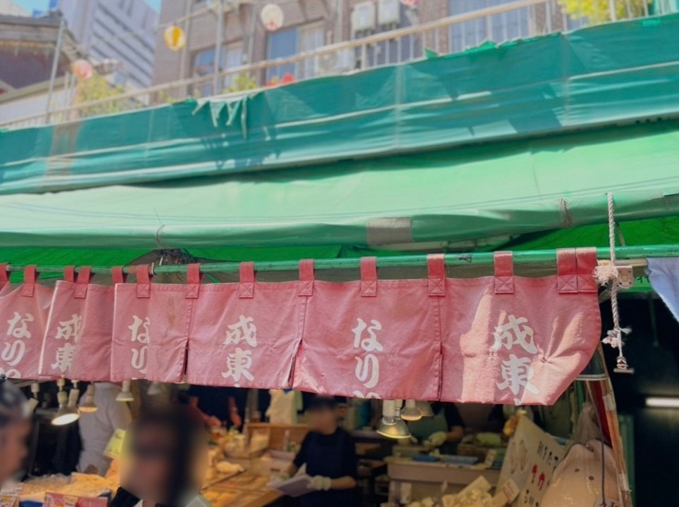 築地場外市場的成東水產店面，紅色布簾與熱鬧攤位吸引民眾停留。