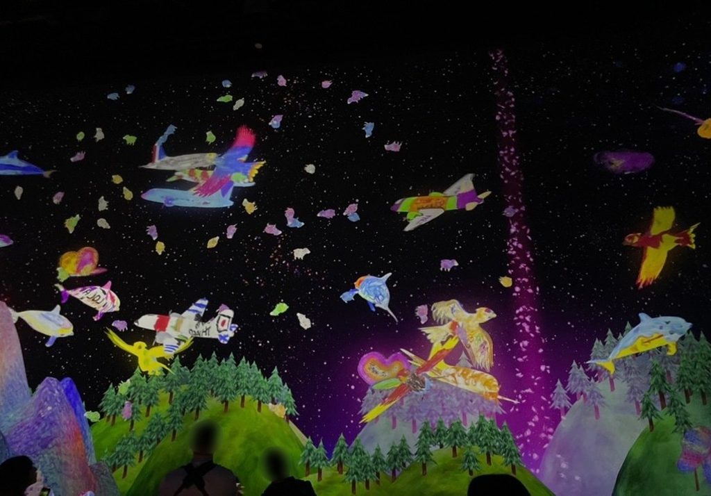 子供が描いた絵をスキャンすると、teamLab Planets の巨大な壁面に投影され、魚や乗り物が自由に動き出すインタラクティブアート。自分の描いたキャラクターが空間を泳ぐ没入型体験。