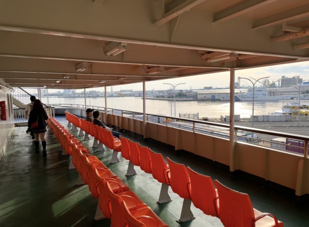 フェリーのデッキ席。オレンジ色の座席が並び、海や港の景色を眺めながら過ごせる屋外エリア。