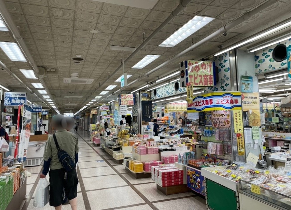 両津港のターミナル内に並ぶ土産店の売り場。棚いっぱいに商品が並び、買い物客が通路を歩くにぎやかな雰囲気の写真。