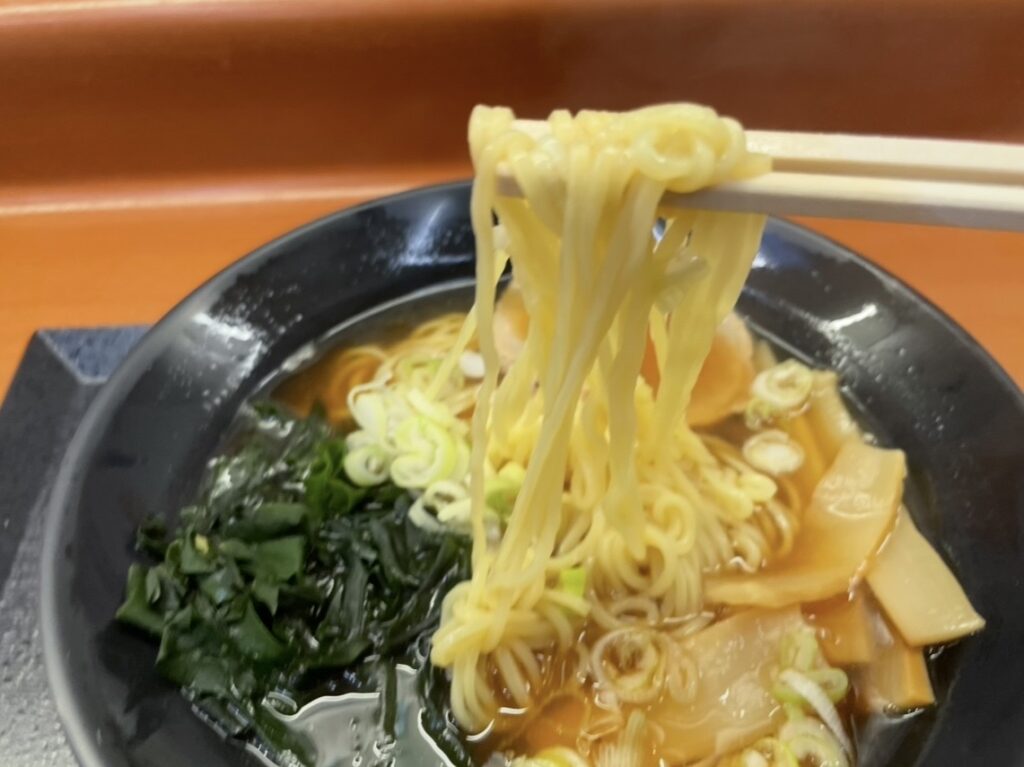 黒い器に盛られたあごだしラーメン。湯気の立つスープに麺が沈み、箸で持ち上げた麺、刻みねぎ、海苔、メンマが彩りを添える写真。