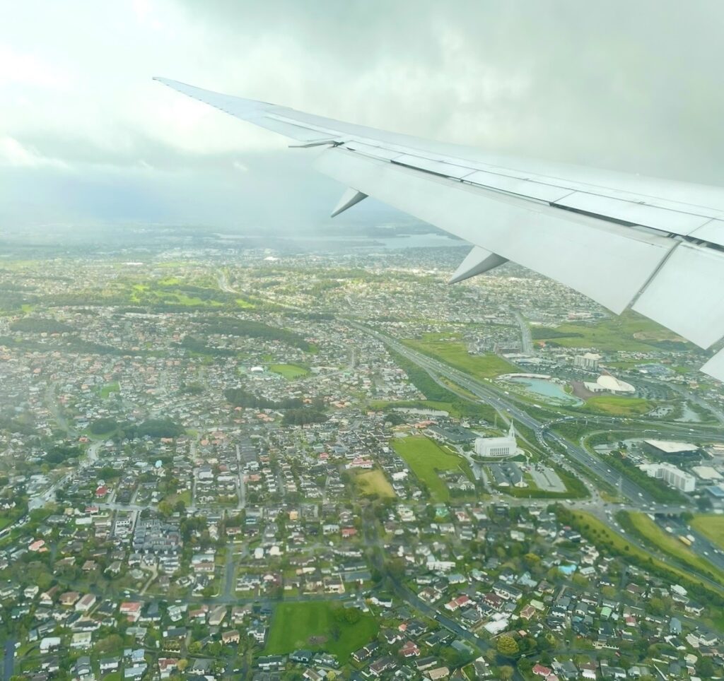 飛行機の翼越しに見えるオークランドの街並み。住宅地や道路が広がる都市景観を上空から撮影した、ニュージーランド航空フライト中の空撮写真。