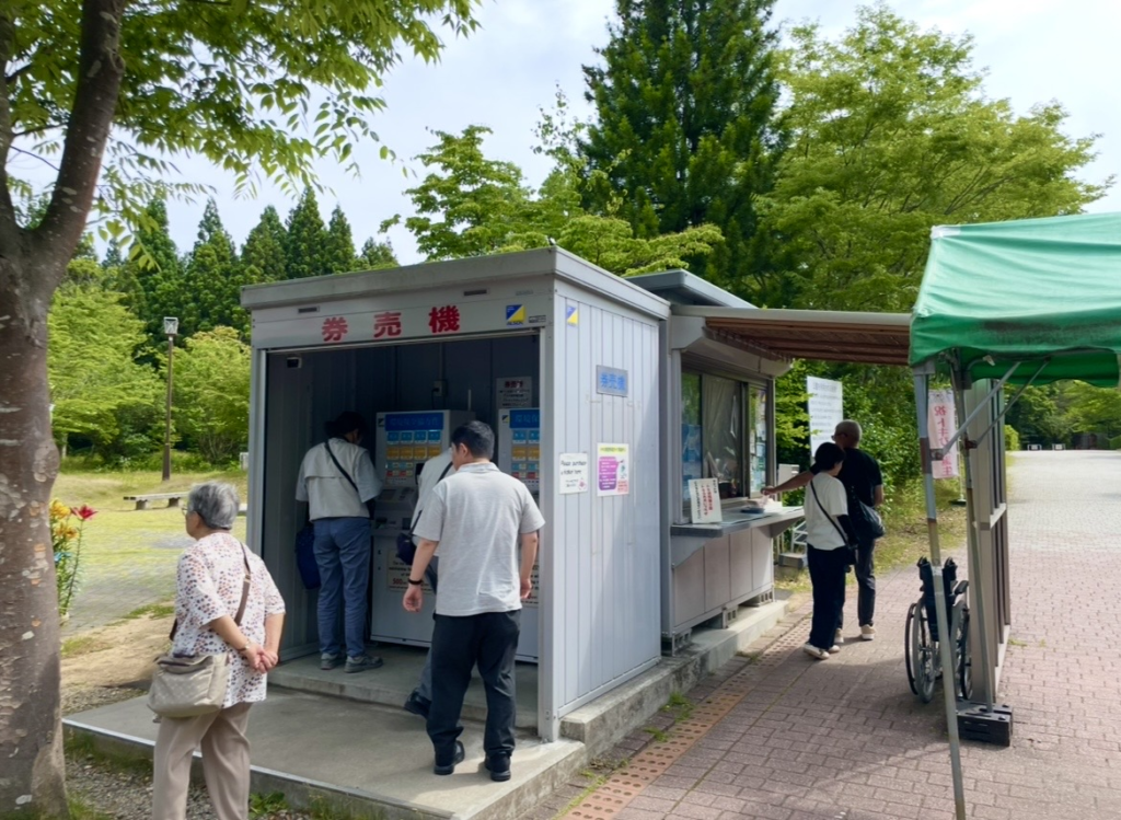 朱鷺之森公園的售票機與售票窗口實景，可見旅客在售票機前購買門票，周邊被綠意環繞的售票區一併入鏡。