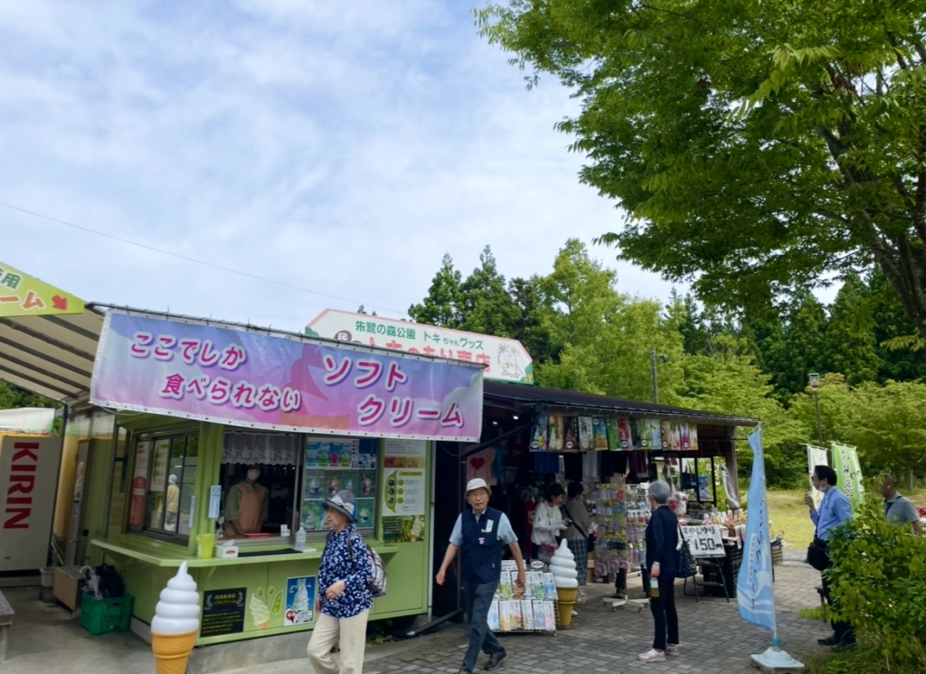 朱鷺之森公園入口附近的販賣店實景，可見販售霜淇淋與輕食的店舖，以及擺放伴手禮的攤位，來訪旅客在周邊散步的樣子一併入鏡。