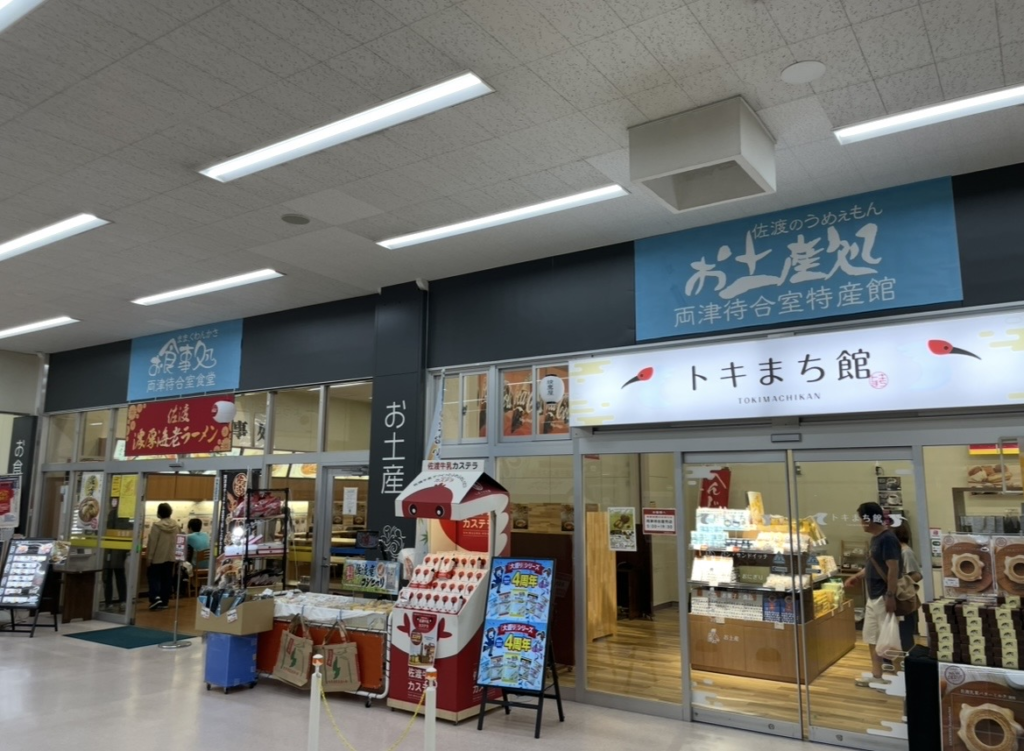兩津港航站樓內的餐飲店與伴手禮店並列，海鮮拉麵的招牌與各式佐渡特產陳列在明亮的店內，呈現地方名物齊聚的景象。