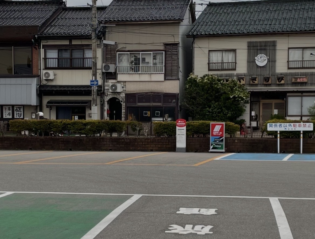 Shuttle pickup area for rental cars in front of Ryōtsu Port. A Nippon Rent‑A‑Car sign stands on the lot, clearly marking the designated pickup point.