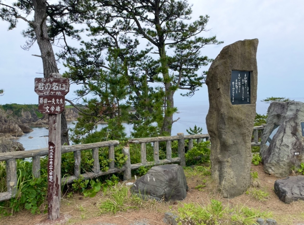 Photo of a literary monument and information board at the Senkaku Bay viewpoint. Set against the dramatic coastal scenery, the markers commemorate the site’s connection to the film Your Name.