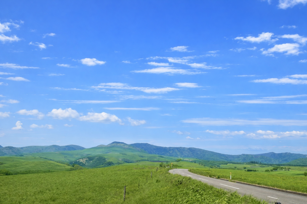 A gently curving road stretches through vast pastureland, with distant hills and mountain ranges extending toward the horizon.
Under a wide blue sky dotted with white clouds, the drive toward Naitai Highland Farm feels open, refreshing, and full of freedom.