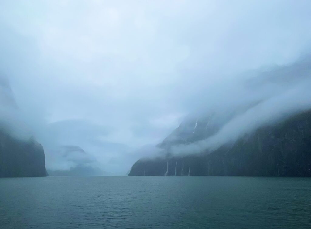霧に包まれたミルフォードサウンドの岩壁と細い滝が流れ落ちる幻想的な冬景色