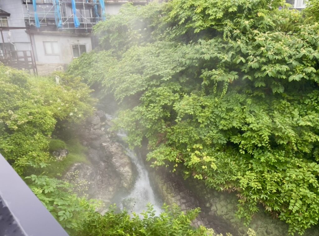 蔵王温泉周辺の自然の中に立ちのぼる温泉の湯気。岩場を流れる湯の流れと緑に囲まれた景観が広がり、温泉地ならではの幻想的で静かな雰囲気が感じられる。