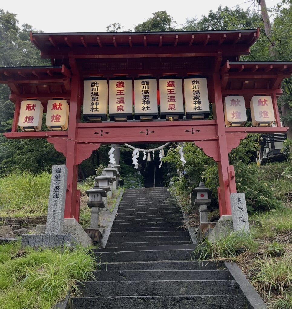 蔵王温泉の酢川温泉神社の赤い鳥居と石段の参道。奉納提灯が並び、木々に囲まれた静かな雰囲気が漂う。