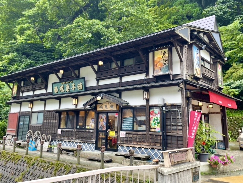 銀山温泉の西塚菓子舗の木造建物。白壁と木枠の外観に和菓子の看板が並び、緑に囲まれた温泉街らしい落ち着いた雰囲気が漂う老舗菓子店。