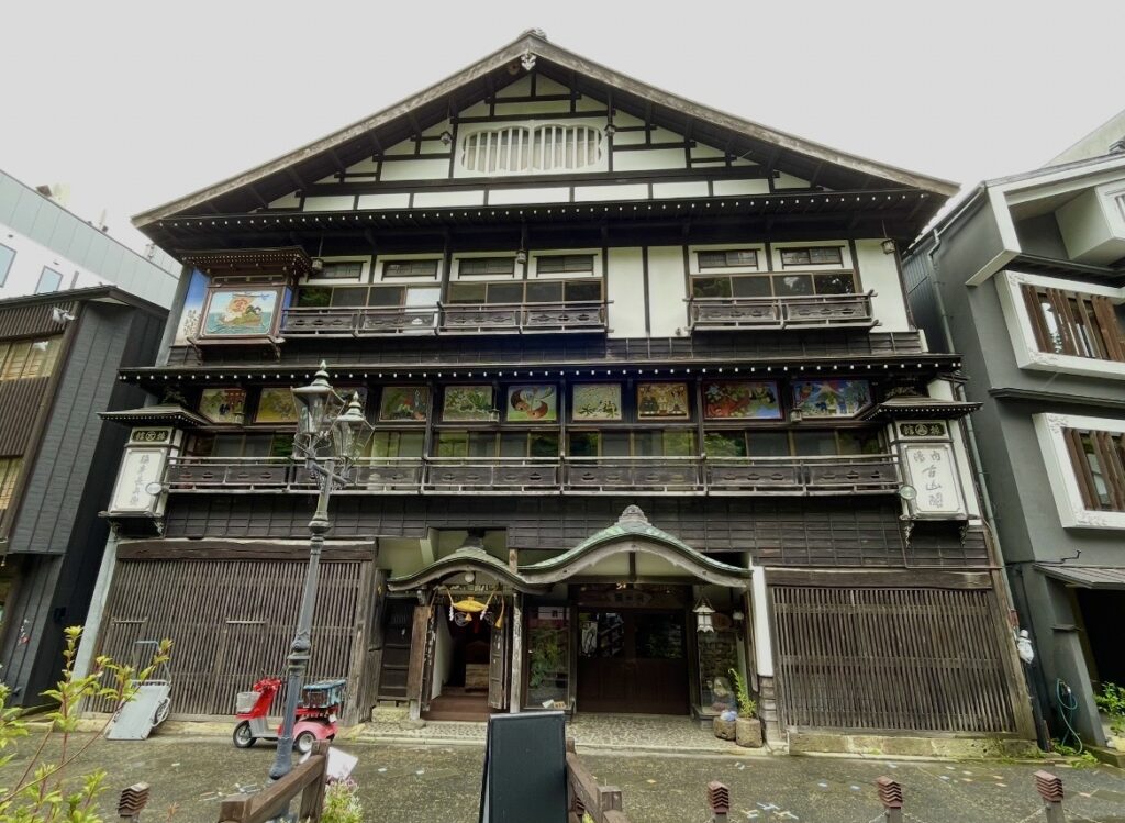 銀山温泉の伝統的な木造旅館。格子窓や装飾パネルが並ぶ重厚な外観と、前に立つ街灯が大正ロマン漂う温泉街の雰囲気を引き立てる。