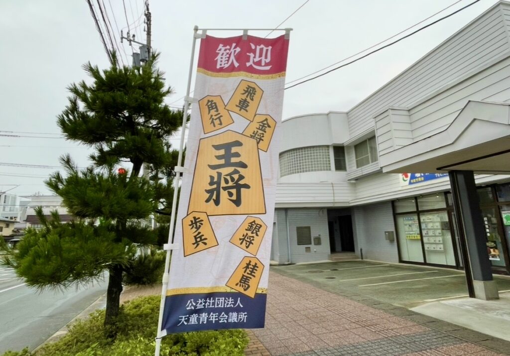 天童の街中に立つ将棋駒が描かれた歓迎の幟。王将や飛車などの駒が並び、将棋のまちらしい雰囲気を伝える街角の風景。