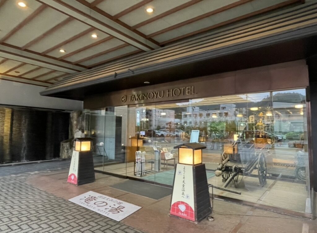 ほほえみの宿 滝の湯のエントランス。ガラス扉と和風の灯籠が並ぶ落ち着いた入口に、木の天井や石造りの外観が調和し、上質な温泉旅館らしい雰囲気を漂わせる。