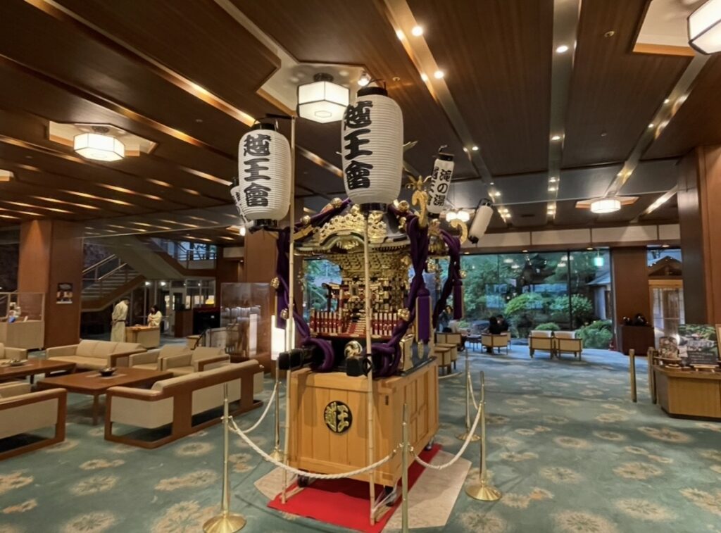 ほほえみの宿 滝の湯のロビーに飾られた神輿とゆとりある館内スペース。天童温泉の文化と旅館らしい雰囲気を伝えるロビーの写真。