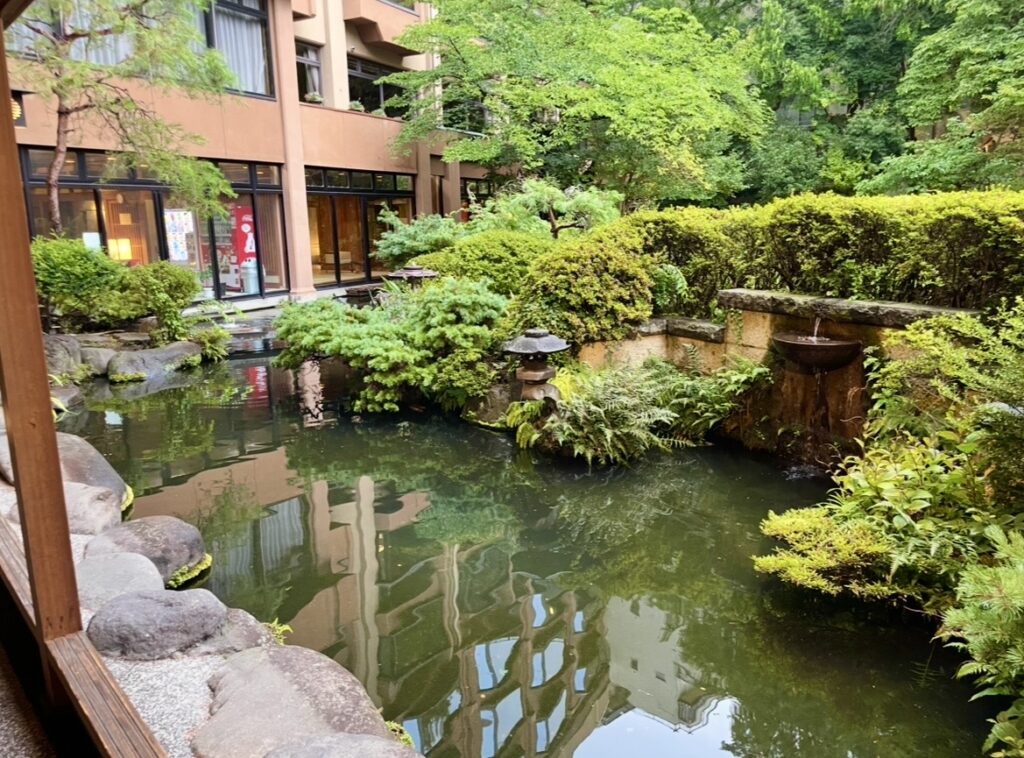 ほほえみの宿 滝の湯の中庭に広がる池と緑豊かな和風庭園。天童温泉の自然美と旅館らしい趣を感じられる中庭の写真。