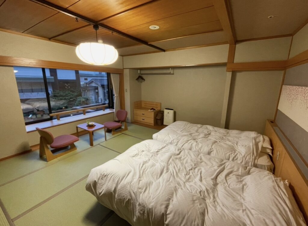 ほほえみの宿 滝の湯の和モダン客室。畳敷きの空間にベッドと窓際の座卓が並ぶ、天童温泉らしい落ち着きある客室の写真。