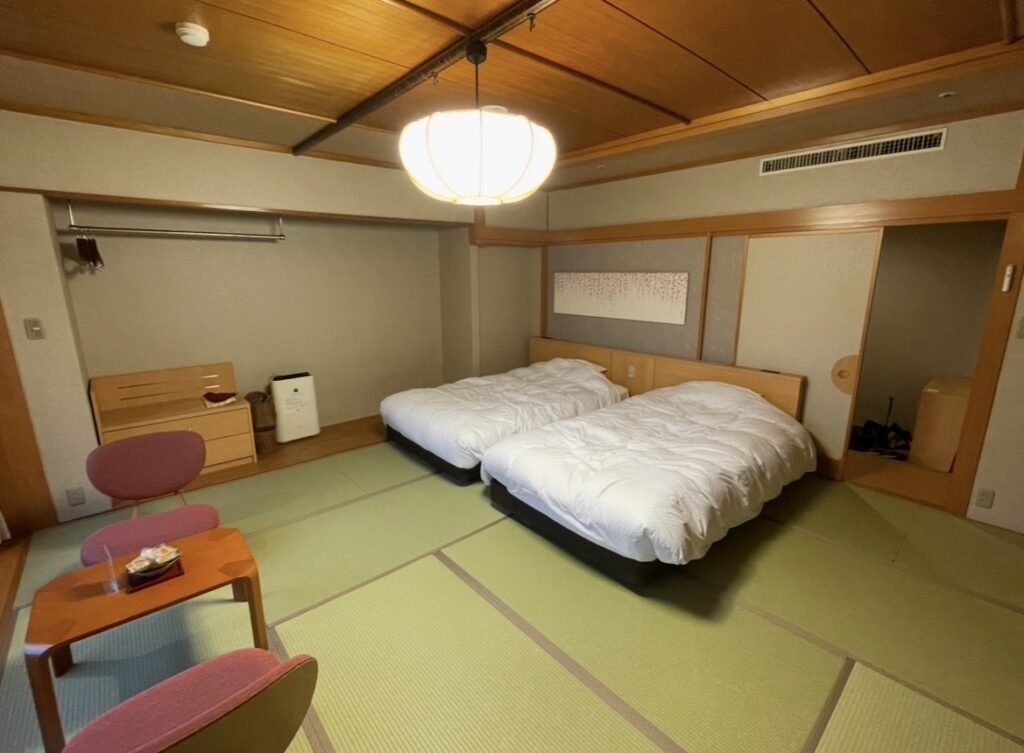 ほほえみの宿 滝の湯の和モダン客室。畳敷きの空間にベッドと窓際の座卓が並ぶ、天童温泉らしい和の趣を感じる客室の写真。