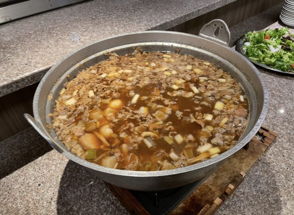 ほほえみの宿 滝の湯の夕食に提供される山形名物・芋煮。牛肉や里芋、野菜を煮込んだ郷土料理が大鍋で温かく仕上がった写真。