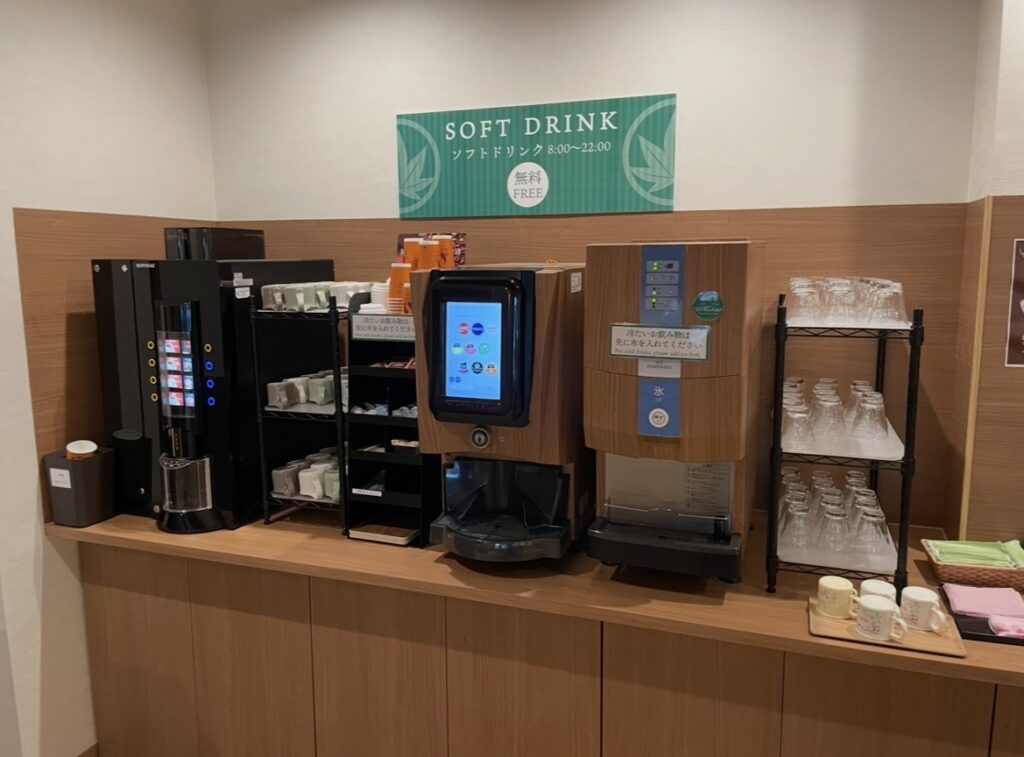 ほほえみの宿 滝の湯のドリンクバー。コーヒーマシンやソフトドリンク機、アイスディスペンサーが並ぶセルフサービスの飲み物コーナーの写真。
