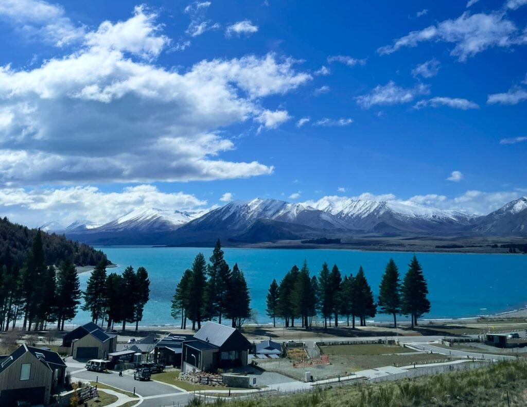 ミルキーブルーのテカポ湖と雪山の絶景。湖畔の住宅街と澄んだ青空が広がるニュージーランド南島の風景