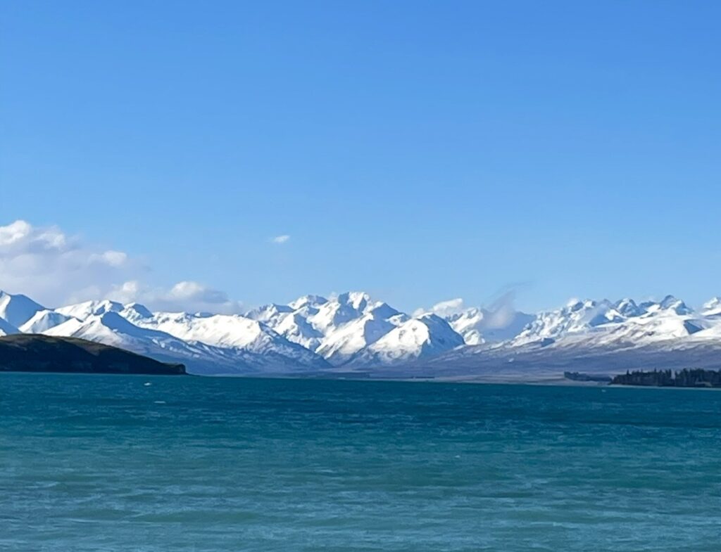 ミルキーブルーのテカポ湖と雪化粧したサザンアルプスが広がる絶景。澄んだ青空の下で輝く湖面と雄大な山々が特徴的なニュージーランド南島の風景