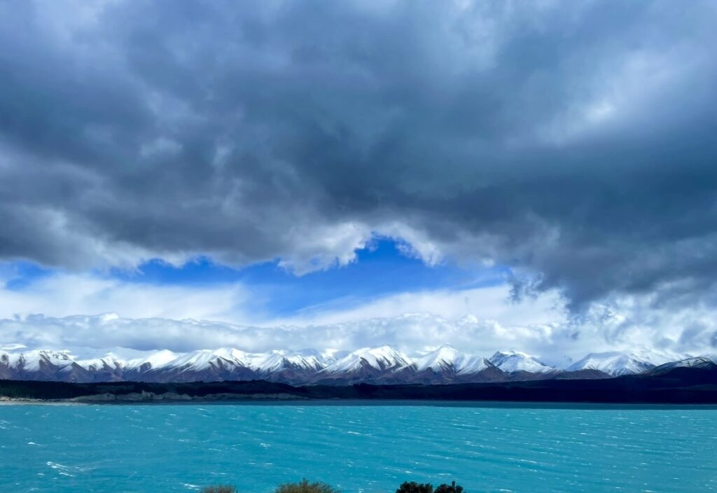 ミルキーブルーのテカポ湖と雪化粧した山々、そして迫力ある雲が広がるニュージーランド南島のダイナミックな絶景