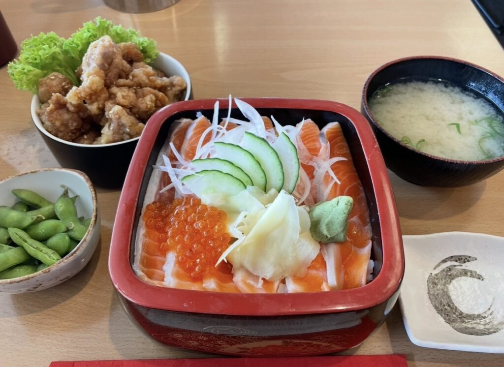 湖畔レストランで提供される新鮮なサーモン丼。脂の乗ったサーモンとイクラが彩りよく盛られ、味噌汁や唐揚げなどのサイドメニューとともに楽しめるテカポ湖の人気グルメ