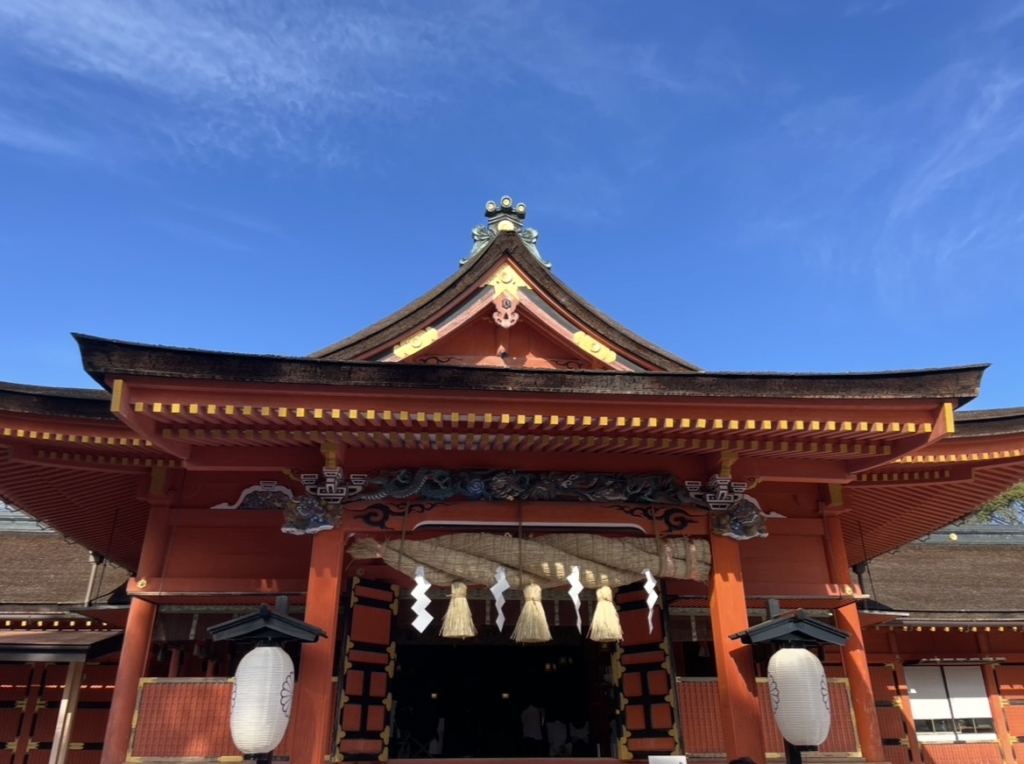 富士山本宮淺間大社的拝殿,鮮紅的建築、巨大的注連繩與精緻木雕十分醒目,入口兩側掛有傳統燈籠,是主要的祭祀空間。
