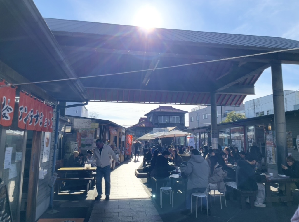 位於富士山本宮淺間大社前的御宮橫丁,美食店林立,戶外座位上坐滿享受富士宮在地料理的遊客,充滿熱鬧氛圍。
