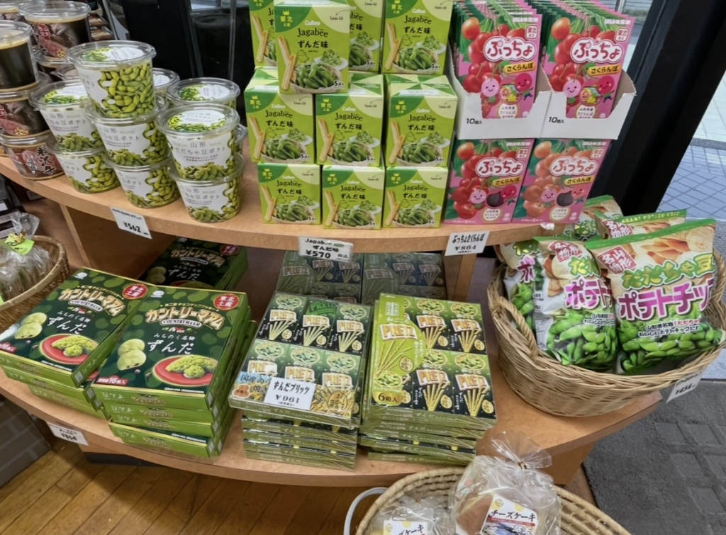 伴手禮店架上陳列著各式枝豆泥風味點心。
像是枝豆 Pretz、枝豆 Country Ma’am、枝豆口味 Jagabee 等綠色包裝商品一字排開，呈現山形名物枝豆泥製品的豐富選擇。