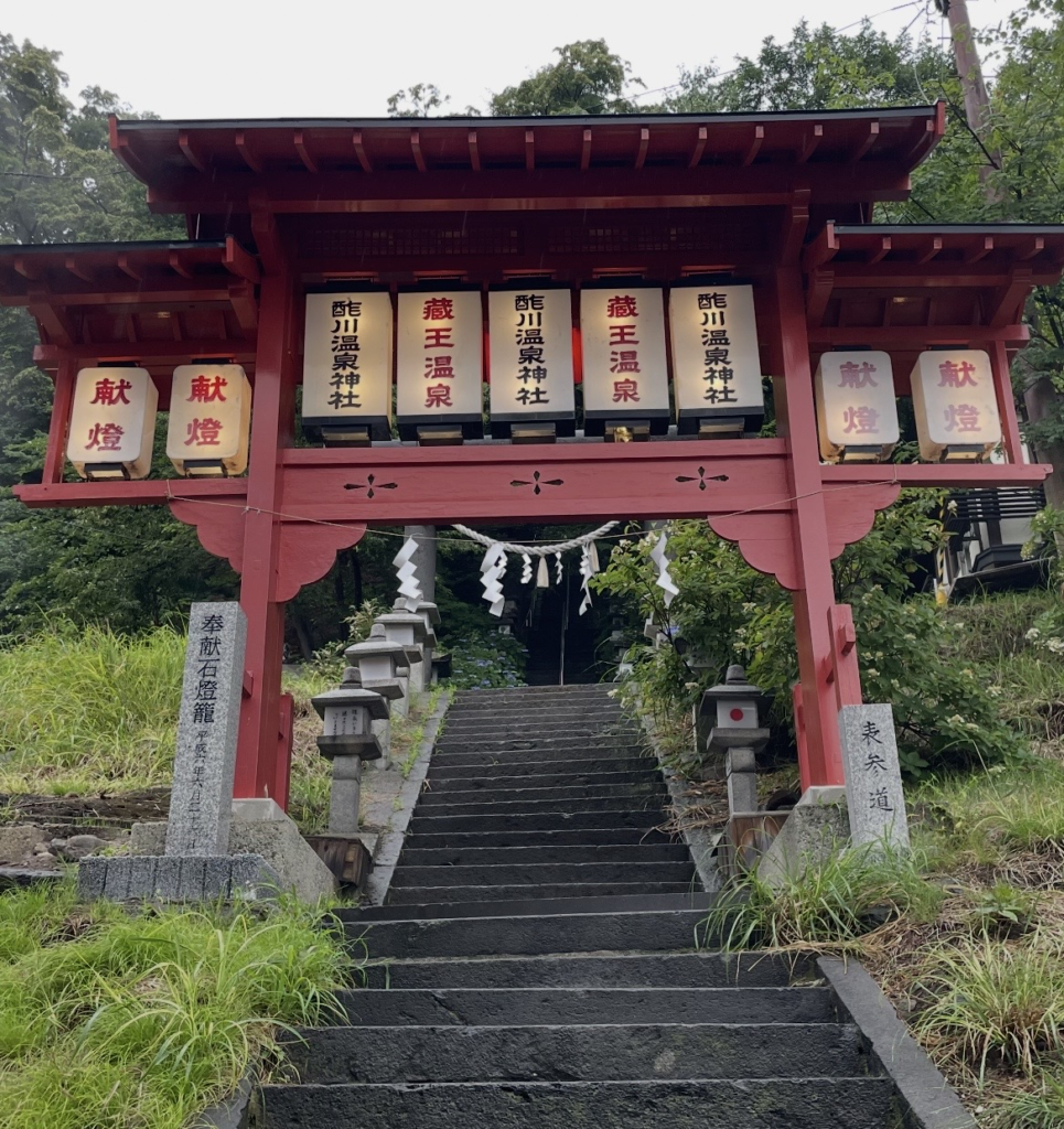 藏王溫泉的酢川溫泉神社紅色鳥居與石階參道。
兩側排列著奉納燈籠，周圍被樹木包圍，散發出寧靜沉穩的氛圍。