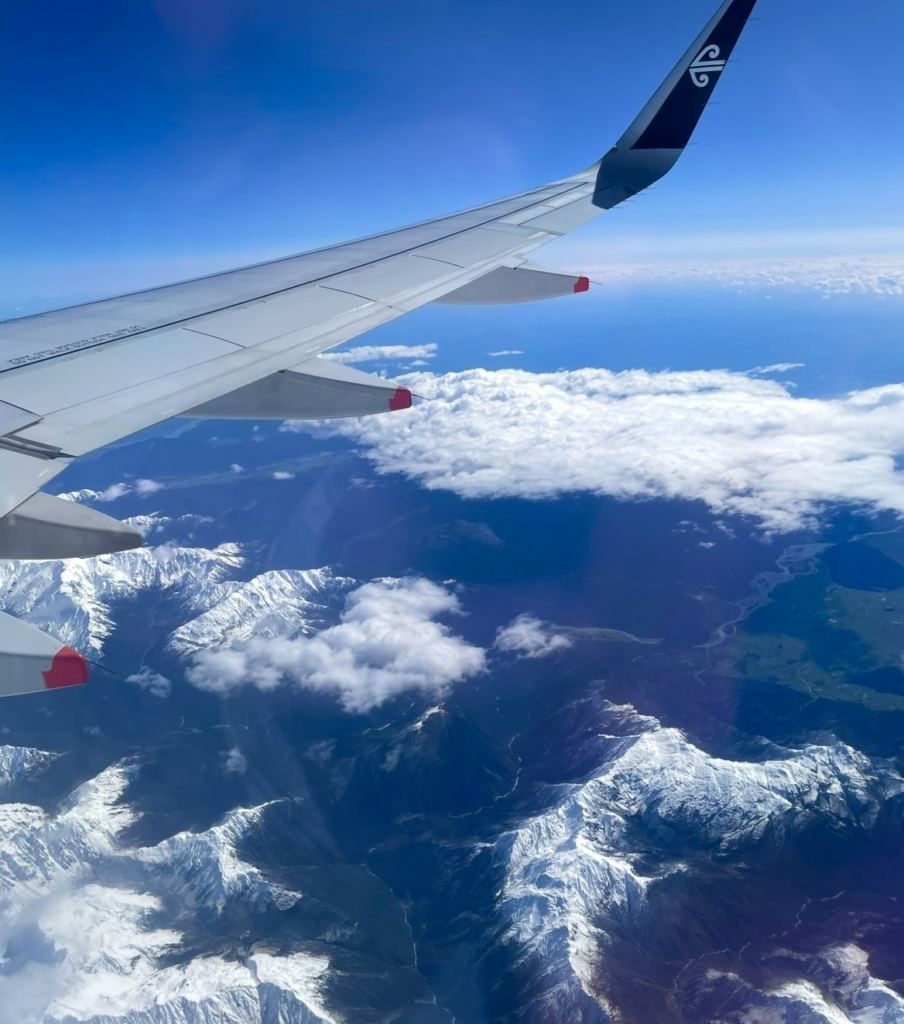 在紐西蘭航空航班上拍攝的壯麗空拍景色。
覆蓋白雪的山脈與雲層延伸在眼前,機翼一同入鏡,展現紐西蘭大自然的震撼風光。