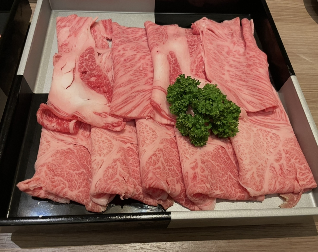 Plated slices of beautifully marbled Yamagata beef. The fine, delicate fat marbling and vibrant parsley accent highlight the premium quality and rich flavor of this renowned Japanese wagyu.