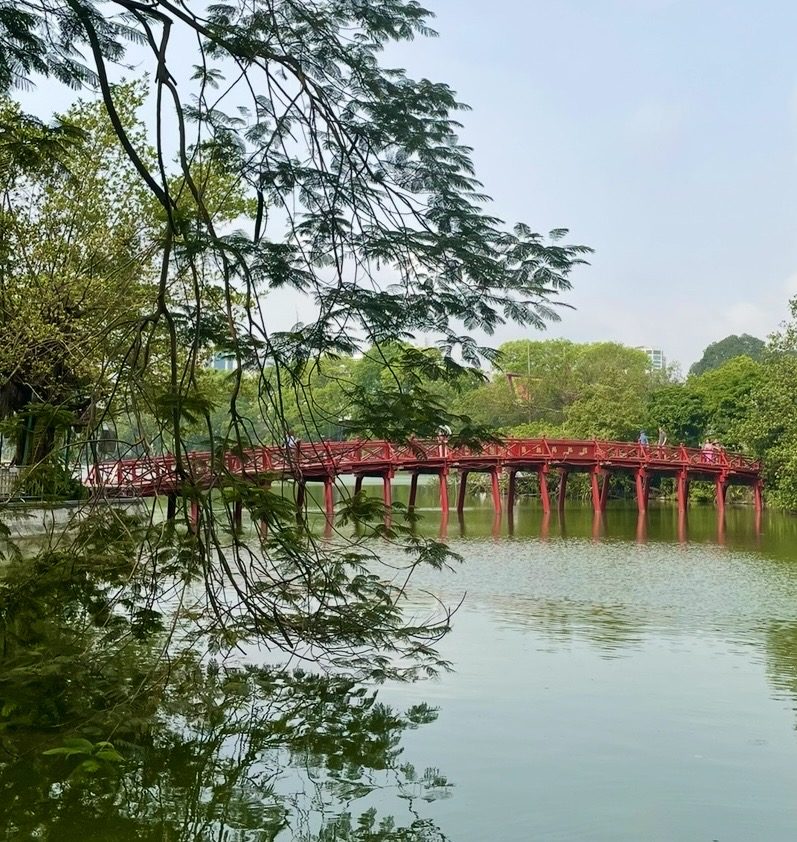Red Thap Rua Bridge over Hoan Kiem Lake surrounded by lush green trees