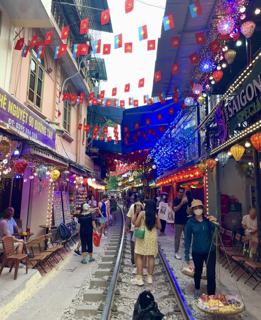 旅客漫步在河內火車街,鐵道兩旁的咖啡館與旗幟營造出熱鬧景致