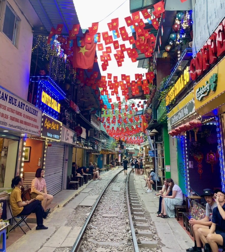 人們在河內火車街鐵道旁坐著休息與林立的咖啡館招牌構成的熱鬧巷弄景致