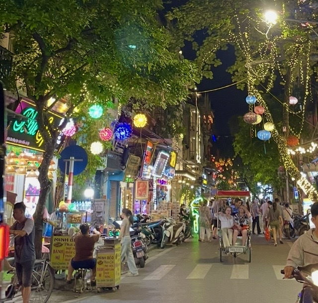 河內舊城區夜晚,霓虹招牌與燈籠閃耀的街道上,攤販與機車排列的熱鬧景象