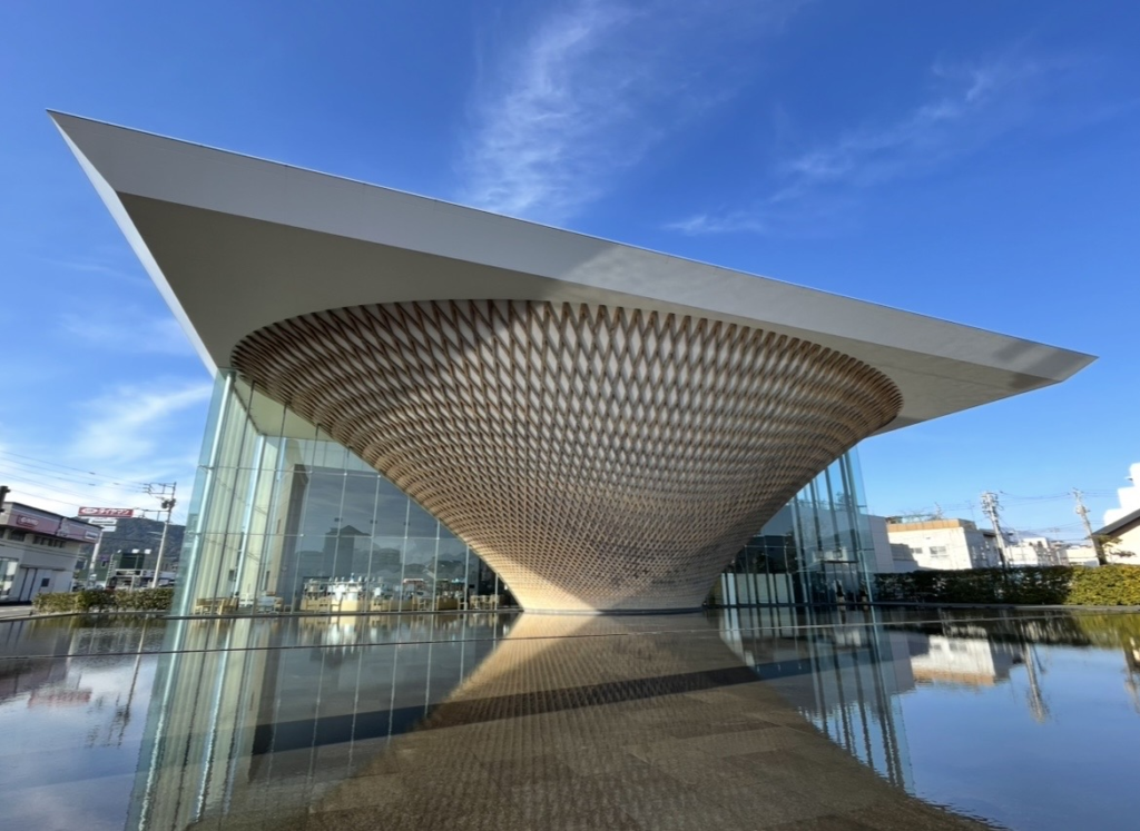 Exterior view of the Mt. Fuji World Heritage Center featuring its iconic inverted-cone wooden lattice design reflected beautifully in the surrounding water. A popular spot to learn about Mt. Fuji’s World Heritage history.