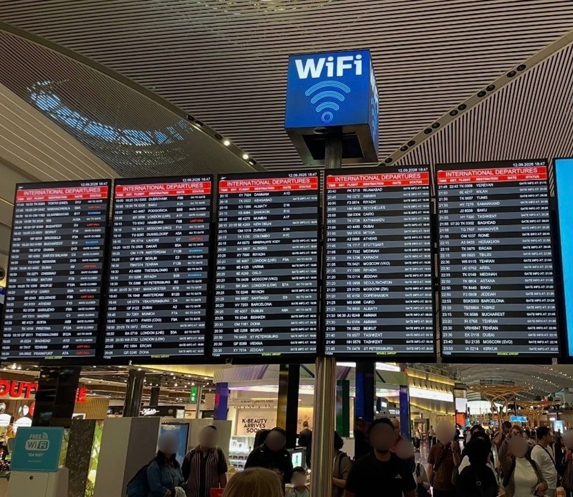 A large electronic departure board in the departure lobby of Istanbul Airport. Rows of international flights are displayed, capturing the movement of travelers and the modern atmosphere of the airport.