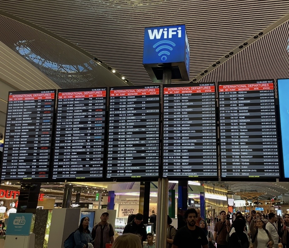 イスタンブール国際空港の出発ロビーに設置された大型電光掲示板。国際線の出発便が並び、行き交う旅行者の姿と近代的な空港の雰囲気が伝わる。