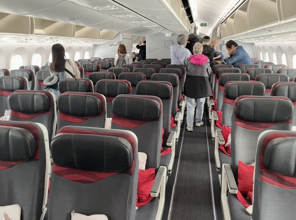 ターキッシュエアラインズの機内エコノミークラス。3-3-3配列のシートが並び、乗客が荷物を収納しながら搭乗準備を進める様子が広がる。
