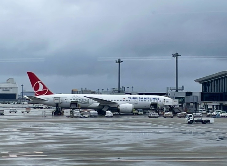 成田空港のスポットで駐機するターキッシュエアラインズ機。雨上がりの滑走路で地上支援車両が行き交い、出発準備が進む様子が伝わる。