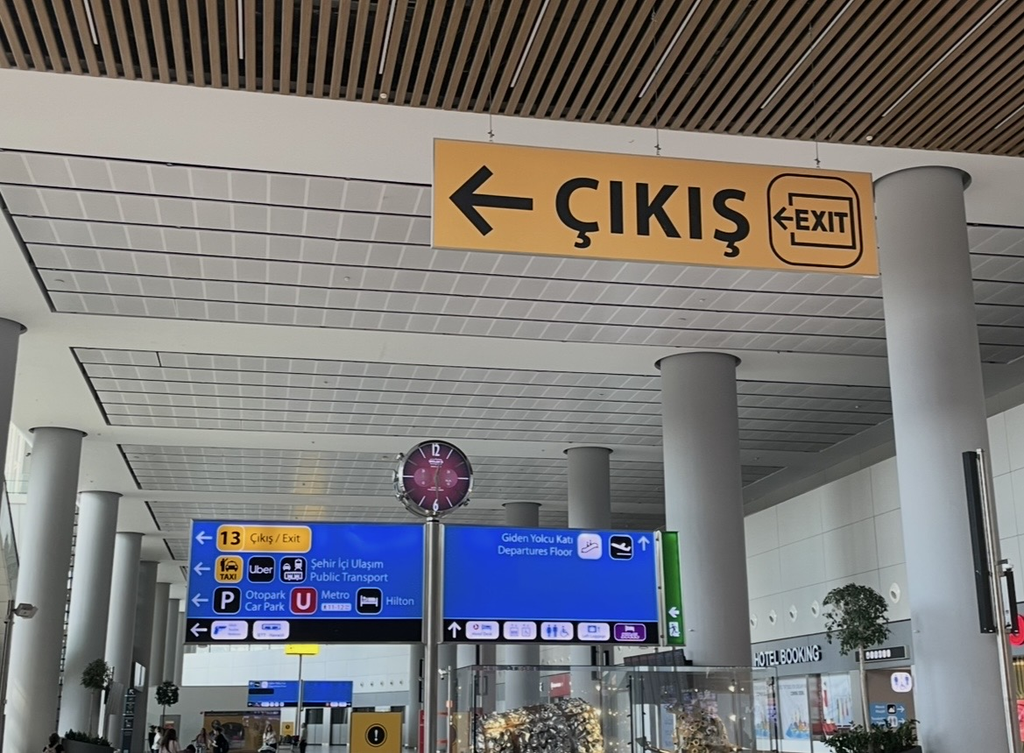 A large “çıkış (exit)” sign displayed in the arrival hall of Istanbul Airport, showing directions to public transportation and taxis for easy navigation within the terminal.
