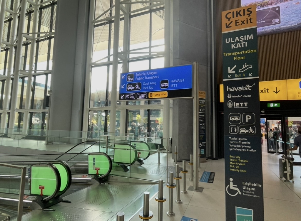 An escalator leading to the Havaist bus boarding area at Istanbul Airport, with clear signage guiding travelers toward public transportation on the connecting floor.
