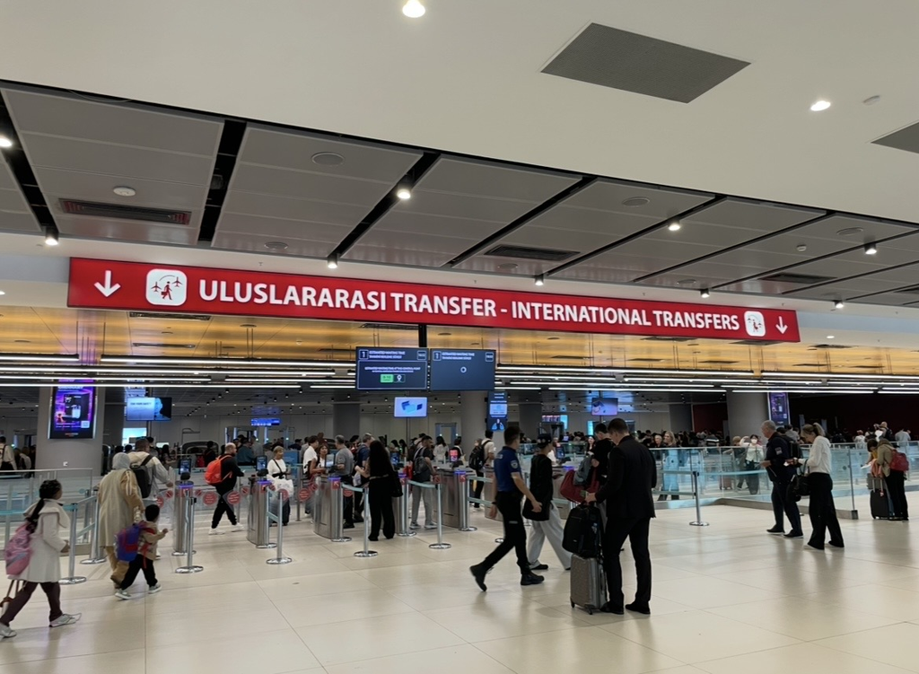 The international transfer area at Istanbul Airport, where travelers move toward the security checkpoint under a red “International Transfers” sign.