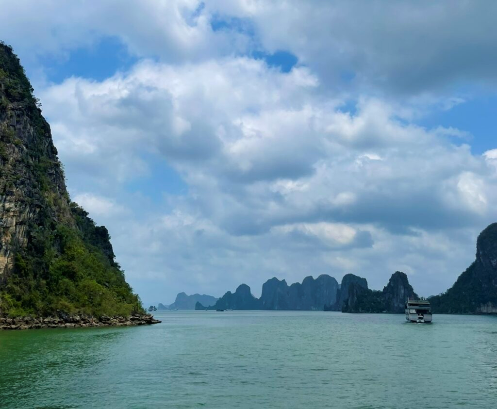遊船航行在下龍灣，穿梭於覆滿綠意的石灰岩奇岩之間，呈現下龍灣特有的雄偉景觀。